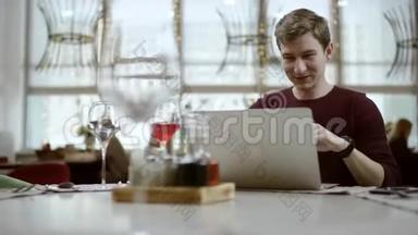 一个年轻的商人坐在一家咖啡馆的桌子旁，用<strong>iphone</strong>一边笑一边看着过路人